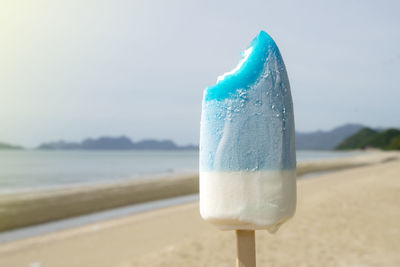 Close-up of drink in sand at beach against sky