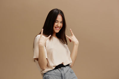 Young woman gesturing peace sign against beige background