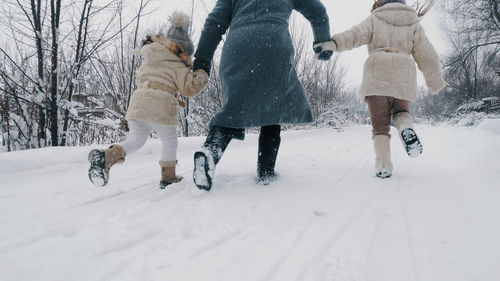 Winter family activity outdoors.. happy woman with 2 daughters are running on snowy road, in forest