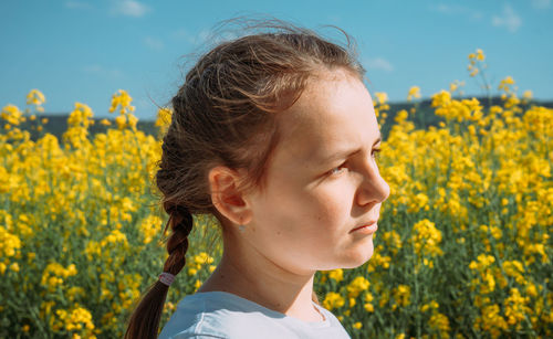 Close-up of young woman standing amidst yellow flowering plants against sky