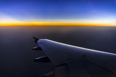 Airplane wing against sky during sunset