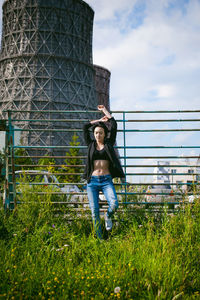 Low angle view of young woman standing by fence against silo