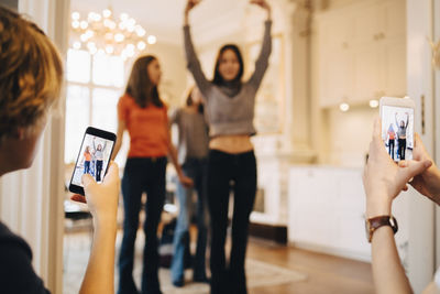 Teenage boys photographing girls through mobile phone dancing at home