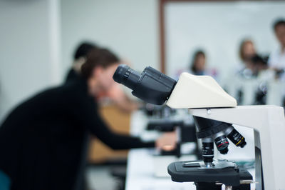 Close-up of microscope with scientists in background at laboratory