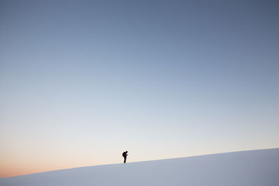 Man standing on snowcapped mountain against clear sky at sunset