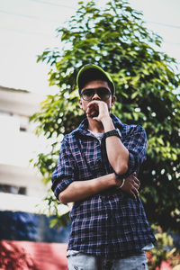 Young man wearing sunglasses standing against plants