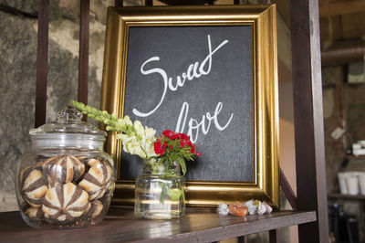 Close-up of blackboard with candies in jar by flower vase on table