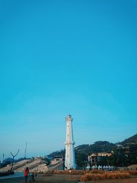 Lighthouse by sea against clear blue sky