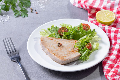 Grilled tuna steak with salad on white dish on concrete table.