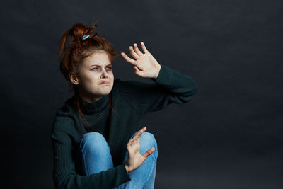 Portrait of young woman standing against black background