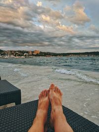 Low section of person relaxing on beach against sky