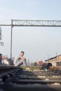 Man sitting on bridge against sky