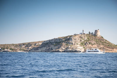 Lighthouse on sea by buildings against clear sky