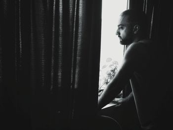 Man looking through window while standing at home