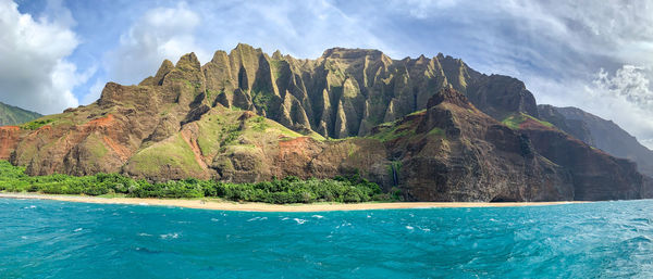 Scenic view of sea by mountain against sky