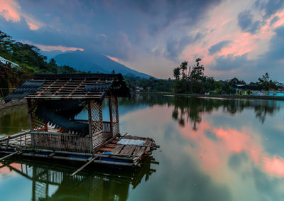Gazebo by lake against sky during sunset