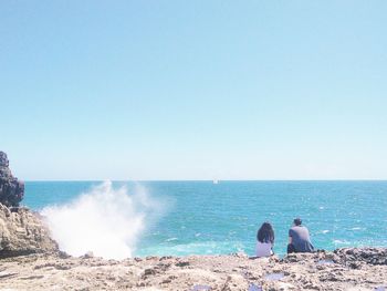 People sitting on beach against clear blue sky