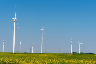 Some wind power plants in a field of flourishing rapeseed seen in germany