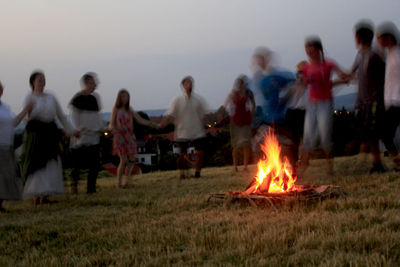 People relaxing on field against sky