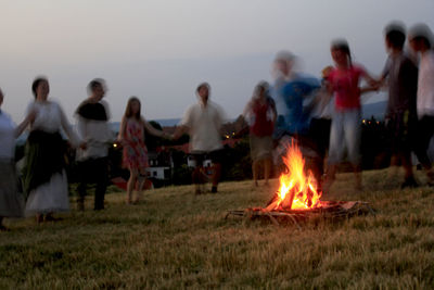 People relaxing on field against sky