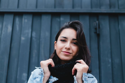 Portrait of smiling young woman standing against wall