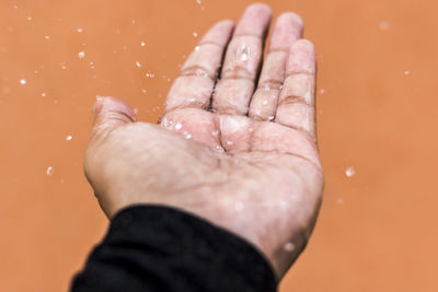 Close-up of water drops falling on hand against wall