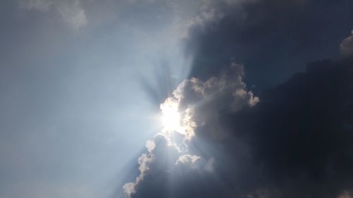 Low angle view of sunlight streaming through clouds