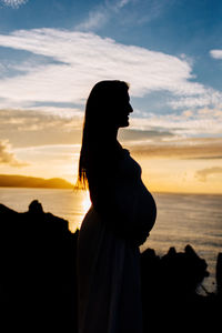 Silhouette woman standing at beach during sunset