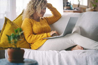 Smiling woman using laptop while sitting on sofa