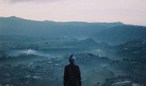 Rear view of man looking at mountains against sky