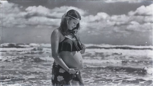 Pregnant woman standing at beach against sky