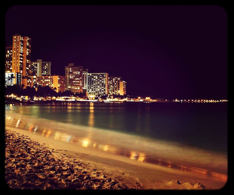 building exterior, water, city, illuminated, architecture, built structure, night, cityscape, sea, beach, clear sky, transfer print, shore, auto post production filter, skyscraper, copy space, urban skyline, river, sky, coastline