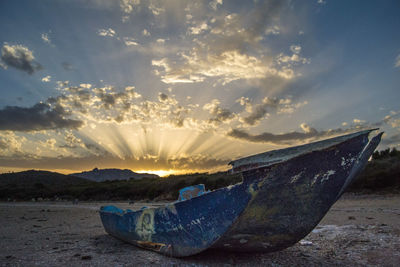 Boat moored on beach against sky during sunset