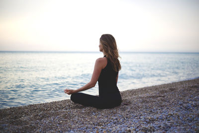 Woman sitting by sea against sky