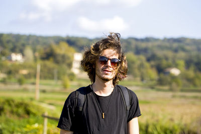Portrait of young man wearing sunglasses while standing at farm against sky