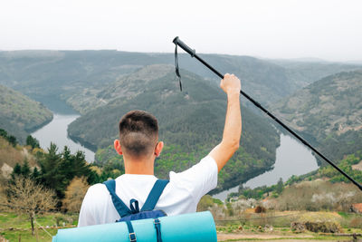 Happy man with backpack raising hands on top