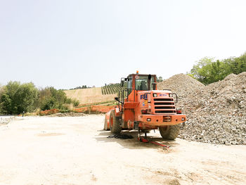 Tractor by heap of stones against clear sky