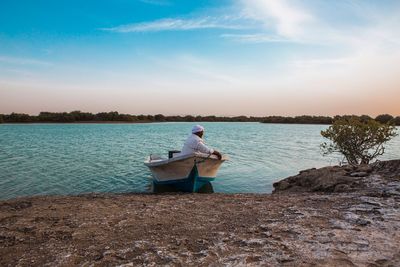 Man sitting on rock by lake against sky