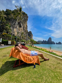 Rear view of woman sitting on beach against sky