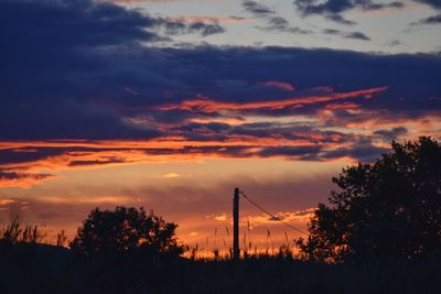 Silhouette trees on field against dramatic sky during sunset