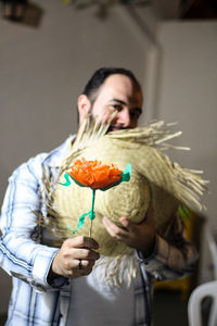 Portrait of man holding straw hat while giving orange paper flower