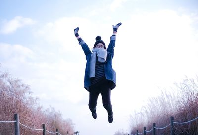 Full length of woman wearing warm clothing while jumping against sky