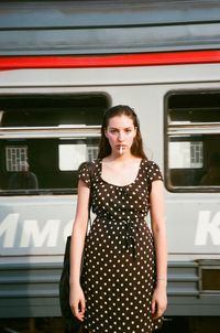 Portrait of young woman smoking cigarette while standing against train