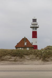 Lighthouse on beach by building against sky