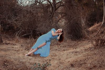 Digital composite image of young woman sleeping on butterflies against bare trees in forest