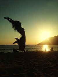 Full length of silhouette woman jumping with arms raised at beach during sunset