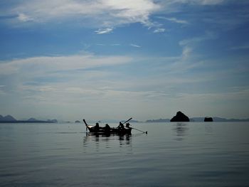 Silhouette people in boat on sea against sky