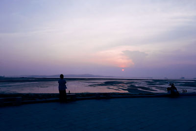 Silhouette people standing on beach against sky during sunset