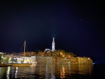 Illuminated buildings by river against sky at night