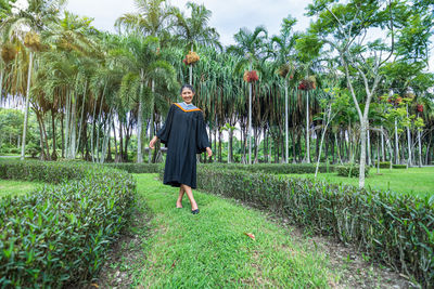 Portrait of woman wearing graduation gown standing on land in park